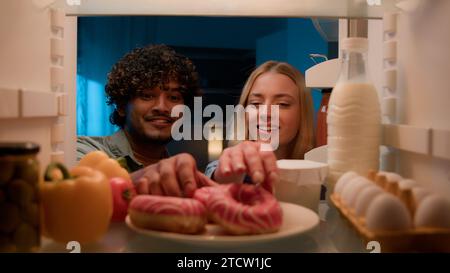 Point de vue POV de l'intérieur réfrigérateur couple multiracial homme indien diverse et femme fille caucasienne à la cuisine de nuit réfrigérateur ouvert manger Banque D'Images