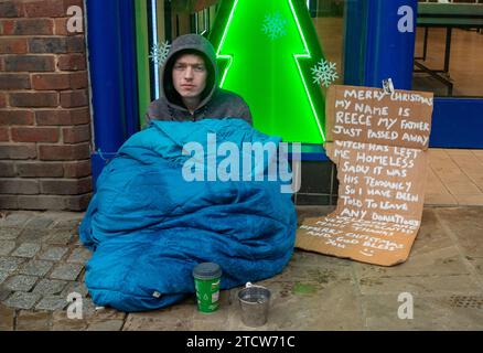 Windsor, Royaume-Uni. 14 décembre 2023. Reece, un homme qui a été rendu sans abri à la suite de la mort de son père, est assis sur le sol froid sous la pluie devant un magasin dans le riche Windsor, Berkshire, espérant que des passants lui donnent des pièces de monnaie. Polly Neate, directeur général de Shelter, a déclaré à Sky News que «le sans-abri n'est sur la liste de Noël de personne, mais 309 000 personnes passeront cette période de l'année dans une minuscule chambre d'auberge ou geler dans une porte». Crédit : Maureen McLean/Alamy Live News Banque D'Images