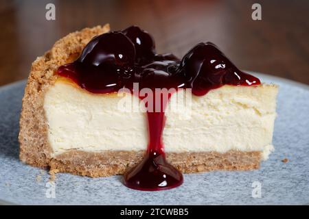 Une portion unique en tranches d'un cheesecake New-yorkais profond garni de cerises noires. Le gâteau est servi en plaque. Banque D'Images