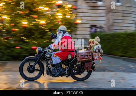 Cottbus, Allemagne. 14 décembre 2023. Un homme habillé comme le Père Noël monte sa moto vintage devant un sapin de Noël illuminé. Crédit : Frank Hammerschmidt/dpa/Alamy Live News Banque D'Images