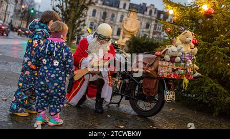 Cottbus, Allemagne. 14 décembre 2023. Un homme habillé en Père Noël écrit les souhaits des enfants dans son «livre de souhaits» tout en agenouillant devant sa moto. Crédit : Frank Hammerschmidt/dpa/Alamy Live News Banque D'Images