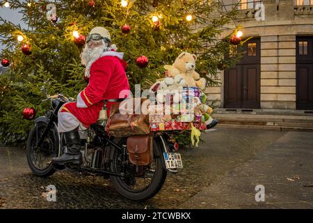 Cottbus, Allemagne. 14 décembre 2023. Un homme habillé comme le Père Noël monte sa moto vintage devant un sapin de Noël illuminé. Crédit : Frank Hammerschmidt/dpa/Alamy Live News Banque D'Images