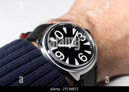 Main masculine avec une montre-bracelet mécanique automatique avec chiffres arabes blancs gras, cadran d'horloge noir et boîtier en acier. Gros plan photo avec sélection de sof Banque D'Images