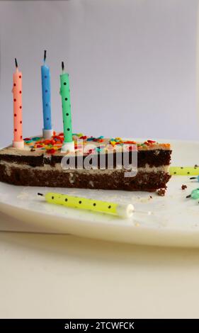 image verticale avec un morceau coupé de gâteau au chocolat au lait avec des bougies d'anniversaire éteintes sur un plat blanc sur un fond clair Banque D'Images