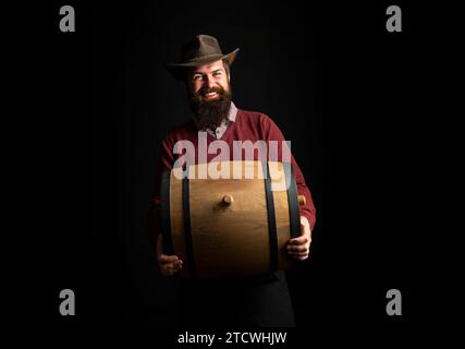 Homme tenir baril en bois sur noir. Oktoberfest. Brasseur barbu. Homme sérieux. Concept de brasserie. Bière pour pub et bar. Fûts de chêne, fût. L'homme porte Banque D'Images