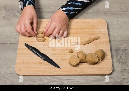 Gros plan une galette de biscuits sucrés à la vanille à partir de pâte crue aux noisettes sur une planche à découper en bois. Les mains féminines forment des biscuits arrondis traditionnels. Banque D'Images