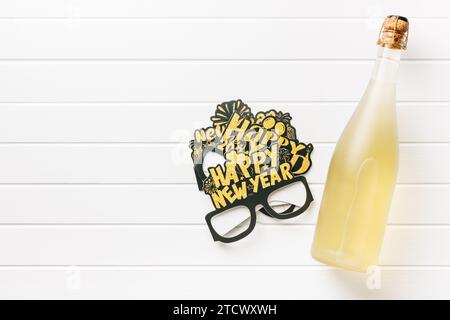 Joyeux fond de nouvelle année. Verres en papier drôles noirs et bouteille de champagne sur la table blanche. Vue de dessus. Banque D'Images