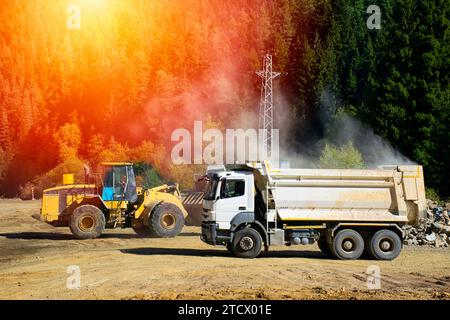 La pelle hydraulique charge la pierre concassée dans une benne de camion à benne basculante. Chargement de pierres sur un camion avec une excavatrice dans la forêt. Banque D'Images