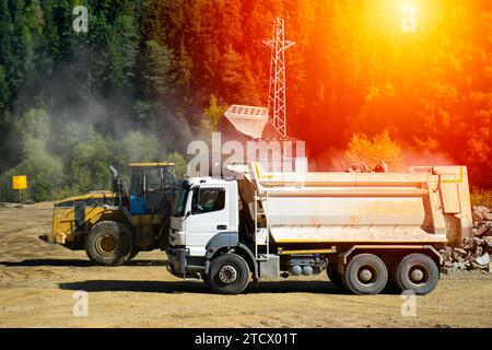 La pelle hydraulique charge la pierre concassée dans une benne de camion à benne basculante. Chargement de pierres sur un camion avec une excavatrice dans la forêt. Banque D'Images