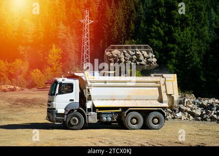 La pelle hydraulique charge la pierre concassée dans une benne de camion à benne basculante. Chargement de pierres sur un camion avec une excavatrice dans la forêt. Banque D'Images