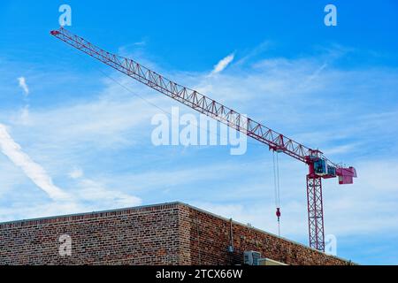 Grue à tour rouge au-dessus du bâtiment en briques contre le ciel rempli de nuages rusés Banque D'Images