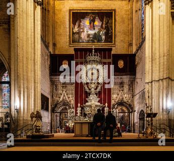 Deux personnes en contemplation devant le retable orné et la grande peinture dans le cadre majestueux de la cathédrale de Séville. Banque D'Images