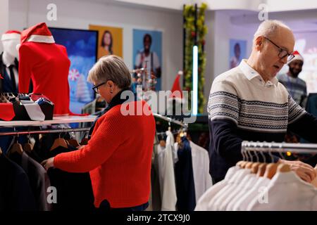 Les personnes âgées regardant des blazers dans le centre commercial, recherchant des vêtements formels sur des cintres avant d'acheter des cadeaux de noël aux membres de la famille. Couple qui va faire du shopping pendant la saison des soldes. Banque D'Images