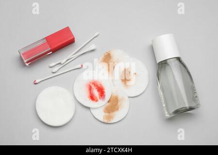 Bouteille de démaquillant, tampons de coton, bourgeons et rouge à lèvres sur fond gris clair, pose plate Banque D'Images