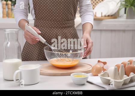 Femme fouettant des œufs dans un bol à la table à l'intérieur, closeup Banque D'Images