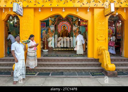 Les visiteurs de Kataragama se tiennent debout avec des offrandes à l'extérieur d'un sanctuaire bouddhiste sur main Street au temple Kataragama au Sri Lanka. Banque D'Images