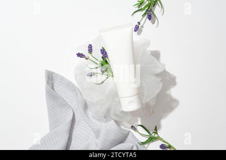 Gros plan d'un tube cosmétique blanc placé sur une éponge de bain avec des fleurs de lavande sur un fond blanc. L'huile essentielle de lavande est utilisée comme toner becau Banque D'Images