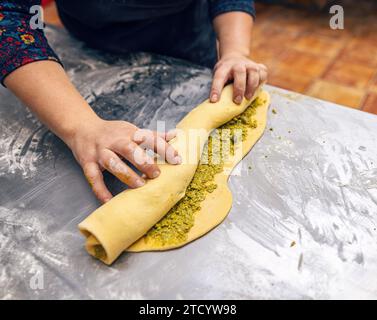 La main de femme roule la pâte farcie pour faire babka. Procédé de boulangerie. Brioche sucrée au rouleau de pistache Banque D'Images