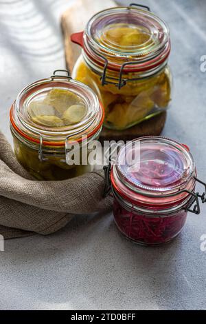 Trois pots avec des légumes fermentés assortis, y compris du chou à la betterave, des poivrons épicés et des concombres blancs, présentés dans un setti de cuisine ensoleillé Banque D'Images