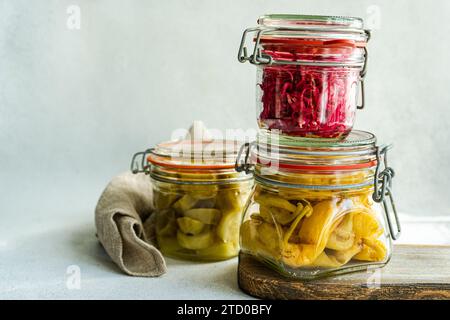 Pots en verre de chou fermenté avec betterave, poivrons épicés et concombres blancs sur une planche de bois. Banque D'Images