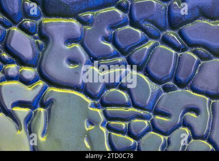 Gros plan d'une surface de sable texturée avec un mélange de teintes bleues et jaunes créant un motif abstrait. Banque D'Images