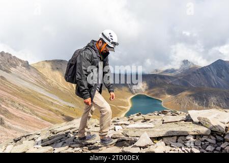 Un randonneur en équipement de sécurité se tient au sommet du terrain accidenté du Nevado de Toluca, contemplant le lac de cratère serein ci-dessous, avec la majestueuse montagne débarrassée Banque D'Images