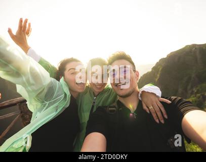 Portrait de jeunes amis caucasiens actifs joyeux prenant selfie regardant la caméra sur le sommet de la montagne au lever du soleil lors de la randonnée de week-end Banque D'Images