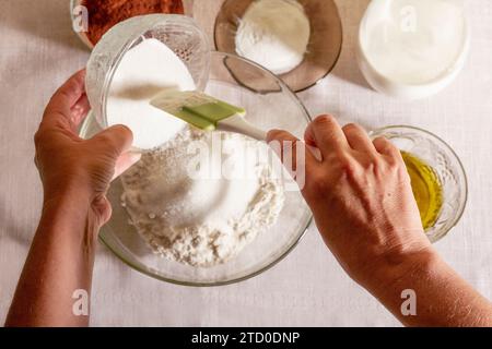 Vue de dessus des mains de la culture anonyme personne versant du sucre dans un bol en verre sur un comptoir de cuisine avec différents ingrédients Banque D'Images