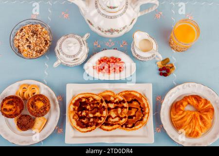 Une variété de plats sains pour le petit-déjeuner soigneusement disposés sur une table bleue, avec du jus d'orange frais et du thé. Banque D'Images