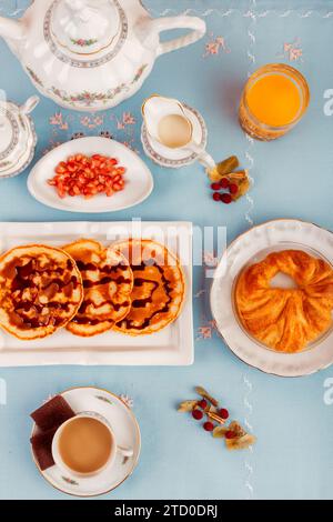 Vue de dessus d'un petit déjeuner continental composé de gaufres, fruits, café et jus de fruits servis sur une surface bleue. Banque D'Images