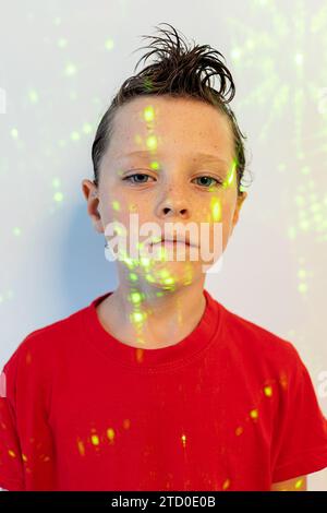 Portrait de garçon confiant en t-shirt rouge avec coiffure regardant la caméra tout en se tenant dans des lumières de néon sur fond blanc Banque D'Images