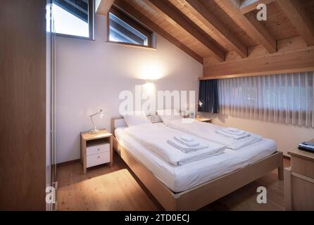 Chambre chalet moderne et accueillant avec poutres en bois, lit double confortable et ambiance lumineuse chaleureuse. Banque D'Images