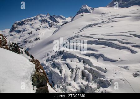 Vue aérienne de skieurs anonymes vêtus de vêtements chauds traversant la surface vierge recouverte de neige d'un glacier contre une montagne rocheuse enneigée Banque D'Images