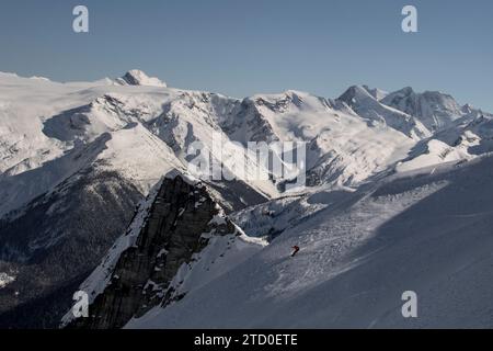 Vue de dessus d'un snowboardeur anonyme descendant sur une majestueuse pente de montagne enneigée contre un ciel bleu clair tout en profitant de vacances d'hiver au Canada Banque D'Images