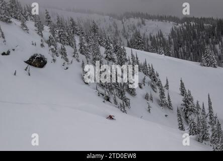 Vue de dessus d'un snowboarder anonyme descendant sur une majestueuse pente de montagne enneigée contre un ciel nuageux clair tout en profitant de vacances d'hiver au Canada Banque D'Images