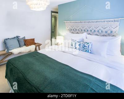 Chambre confortable et élégante avec lit moelleux avec oreillers décoratifs, jeté texturé et suspension élégante. Banque D'Images