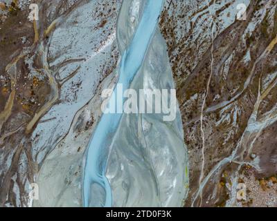 Cette image aérienne capture le chemin complexe d'une rivière glaciaire qui serpente à travers un paysage accidenté et strié de boue, mettant en évidence le conte saisissant Banque D'Images