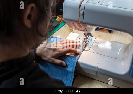 Une photo en gros plan capturant les mains d'une personne alors qu'elle guide le tissu denim à travers une machine à coudre, illustrant le métier de la couture. Banque D'Images