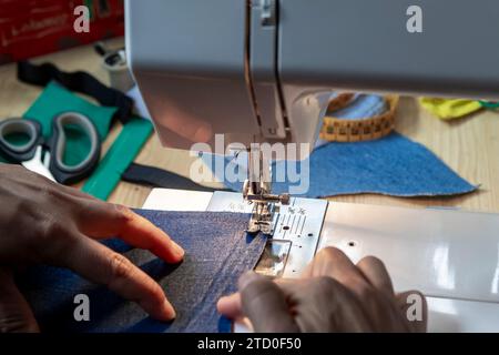 Gros plan des mains guidant habilement le tissu à travers une machine à coudre, avec les essentiels de couture en arrière-plan. Banque D'Images
