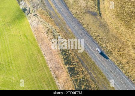 Prise de vue aérienne d'une voiture solitaire traversant une route sinueuse au milieu des paysages contrastés de la vallée de Thorsmork dans les Highlands accidentés d'Islande Banque D'Images