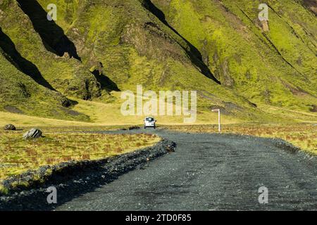 Vue arrière d'une voiture solitaire voyageant le long d'une route sinueuse au milieu des pentes verdoyantes et vibrantes de la vallée de Thorsmork en Islande, mettant en valeur le beau intact Banque D'Images
