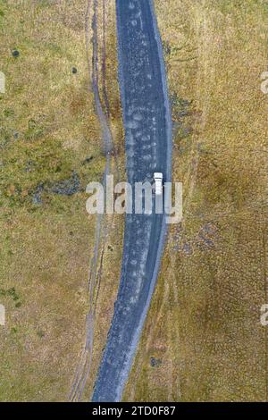 Une photo aérienne capture une voiture solitaire aux portes ouvertes sur une route sinueuse au milieu des vastes paysages texturés des Highlands islandais, près de Thorsmo Banque D'Images