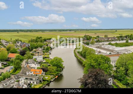 Vue aérienne de la rivière pittoresque qui coule à travers le village entouré de verdure luxuriante et maisons rustiques sous un ciel nuageux Banque D'Images