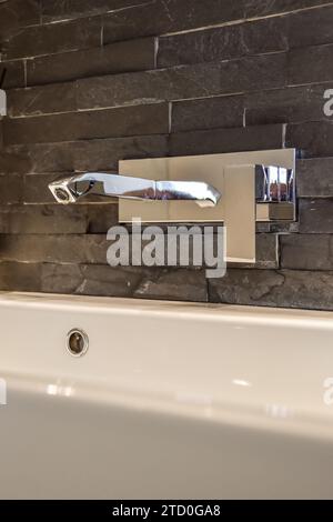 Robinet en acier inoxydable monté sur le mur au-dessus de l'évier en céramique blanche dans la salle de bains de luxe de l'appartement Banque D'Images