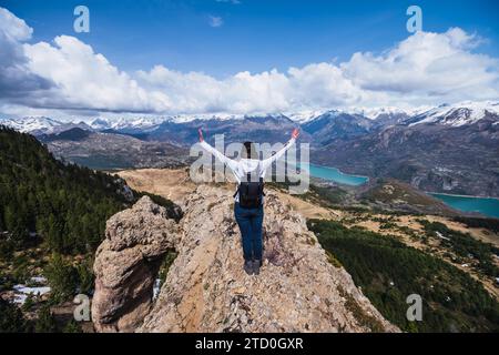 Une femme triomphe sur une crête rocheuse aux bras tendus, surplombant une vue panoramique de montagnes et un lac dans le parc national d'Ordesa, dans les Pyrénées Banque D'Images