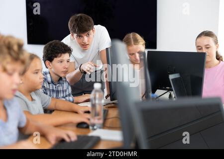 Enseignant homme positif avec le garçon enseigne comment travailler sur ordinateur Banque D'Images