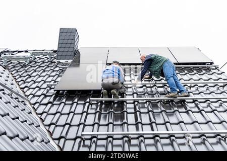 Deux techniciens travaillant à l'installation d'un système photovoltaïque sur le toit d'une maison Banque D'Images