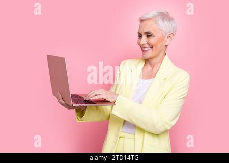 Photo souriant stratégie marketing analytique femme d'affaires en costume jaune tenir un ordinateur portable écrivant des lettres d'email isolé sur fond de couleur rose Banque D'Images