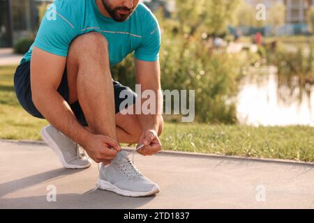 Homme nouant des lacets avant de courir dans le parc, gros plan. Espace pour le texte Banque D'Images