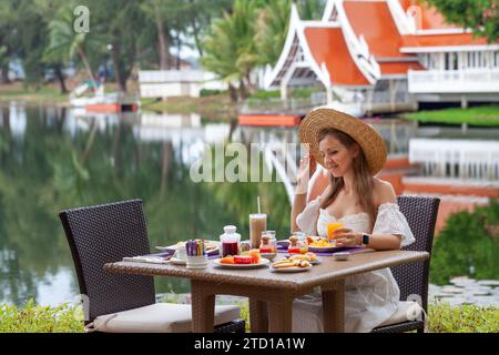 Femme profitant du petit déjeuner à la station tropicale avec vue sur le lac. Banque D'Images